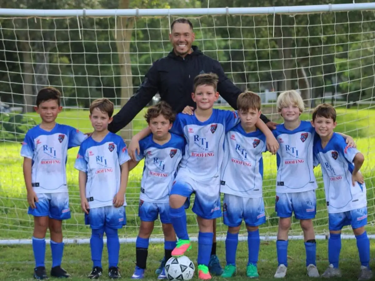 Boys youth soccer team in blue RTI Roofing jerseys posing with their coach in front of a goal