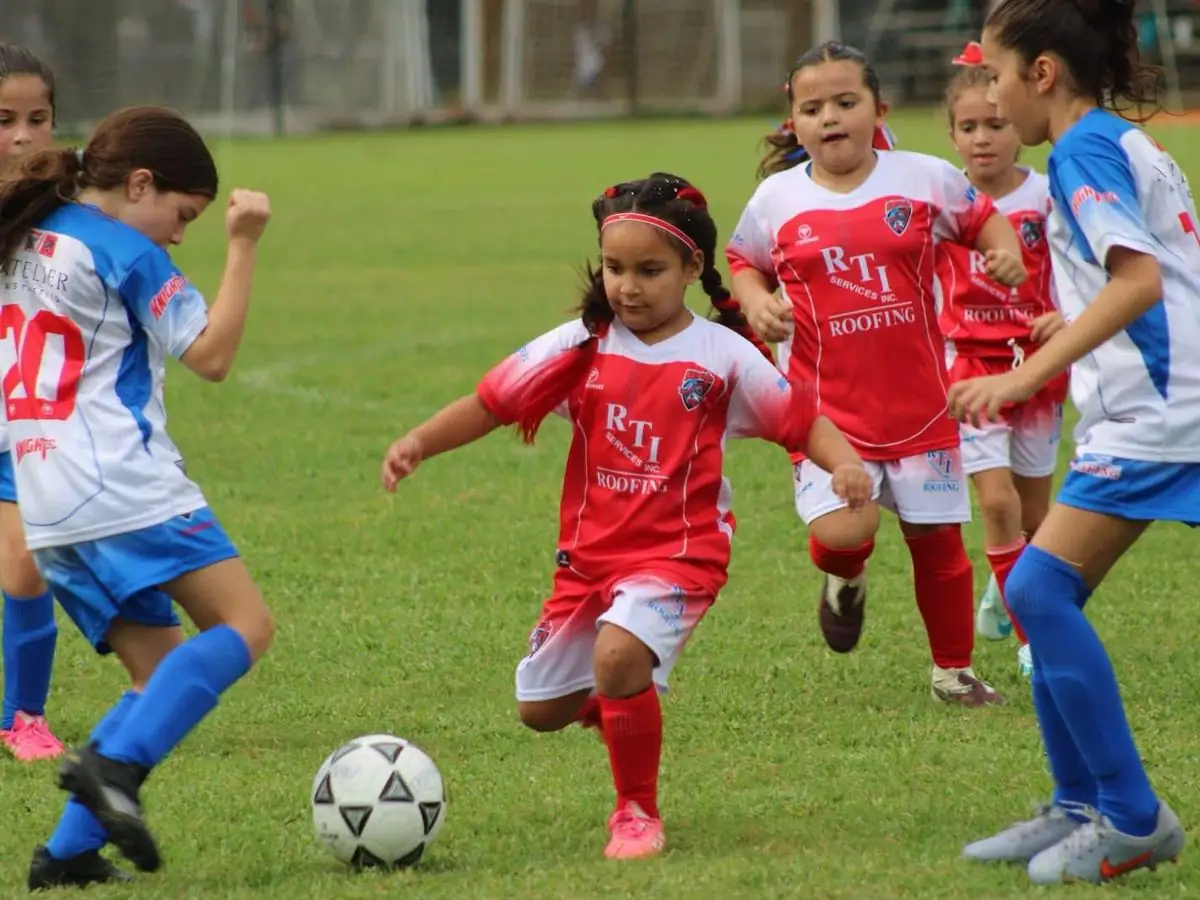 Girls in red RTI Roofing jerseys playing a youth soccer match against a team in blue